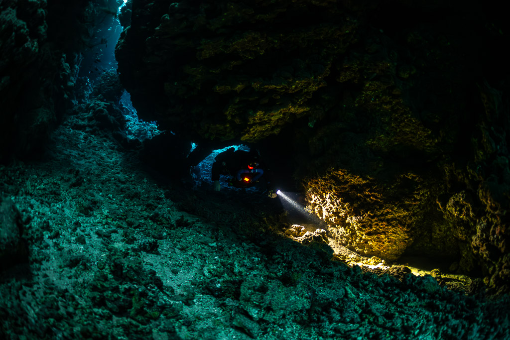 Rebreather diver lighting golden encrustations on the cave wall, Sha'ab Claudio, Red Sea, Egypt