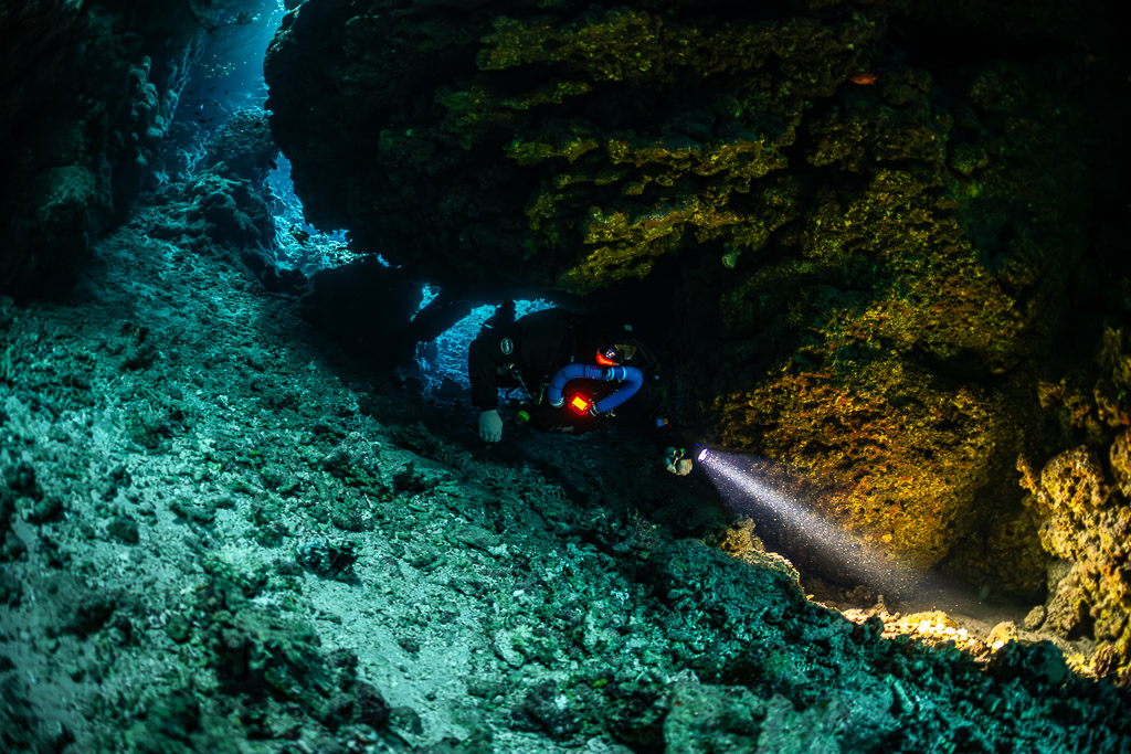 Rebreather diver close-up lighting the golden cave wall, Sha'ab Claudio, Red Sea, Egypt