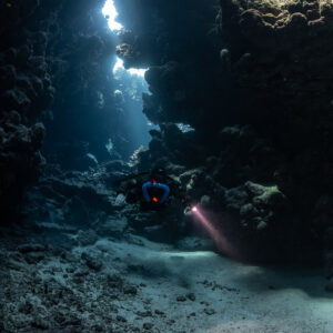 Rebreather diver below a column of skylights, pink torch beam, Sha'ab Claudio, Red Sea, Egypt