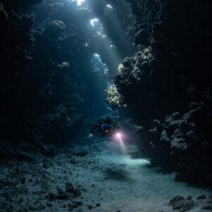 Rebreather diver under sunbeams in a cave gallery, distant, Sha'ab Claudio, Red Sea, Egypt