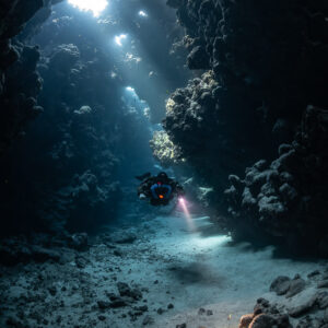 Rebreather diver under sunbeams in a cave gallery, torch on the rocks, Sha'ab Claudio, Red Sea, Egypt