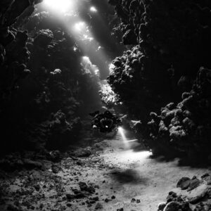 Rebreather diver under sunbeams in a cave gallery, black and white, Sha'ab Claudio, Red Sea, Egypt