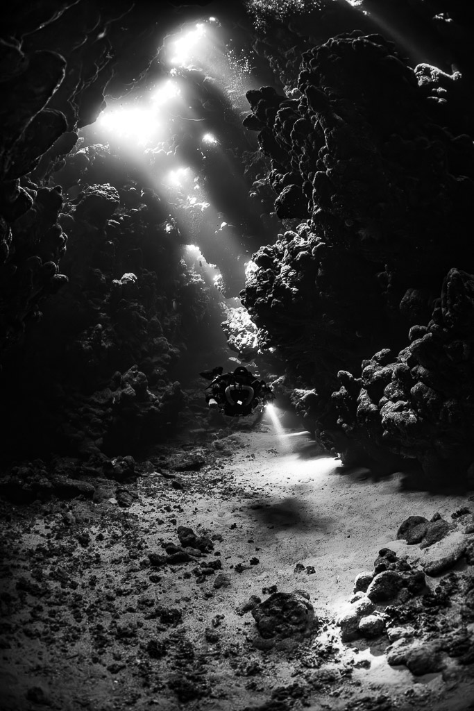 Rebreather diver under sunbeams in a cave gallery, black and white, Sha'ab Claudio, Red Sea, Egypt