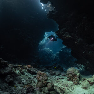 Rebreather diver framed in a distant cave opening, rubble in front, Sha'ab Claudio, Red Sea, Egypt