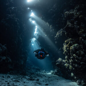 Rebreather diver below a cascade of sunbeams in a narrow gallery, Sha'ab Claudio, Red Sea, Egypt
