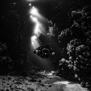 Rebreather diver below a cascade of sunbeams, black and white, Sha'ab Claudio, Red Sea, Egypt