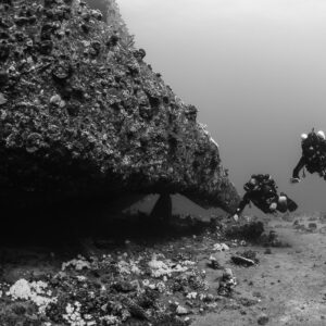 Black-and-white shot of two rebreather divers beside an overhanging hull, Red Sea, Egypt