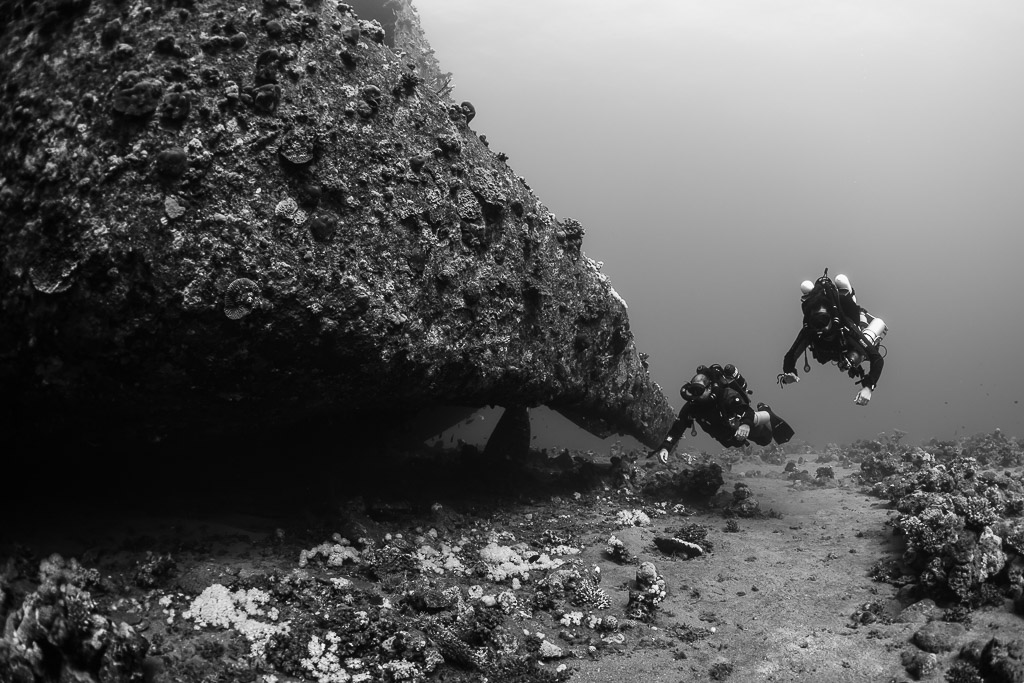 Black-and-white shot of two rebreather divers beside an overhanging hull, Red Sea, Egypt