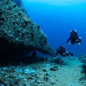 Two rebreather divers approaching the curved hull of a wreck, Red Sea, Egypt
