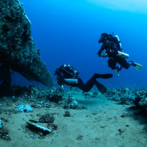 Two rebreather divers swimming close beneath an overhanging wreck hull, Red Sea, Egypt