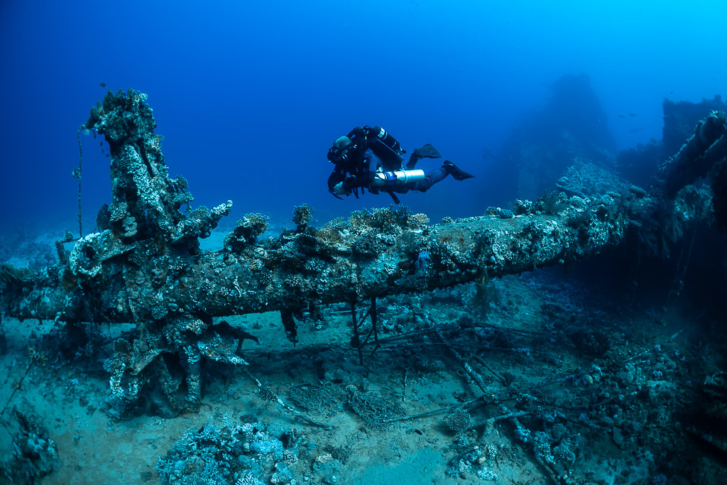 Rebreather diver gliding above an overgrown propeller shaft on a wreck, Red Sea, Egypt