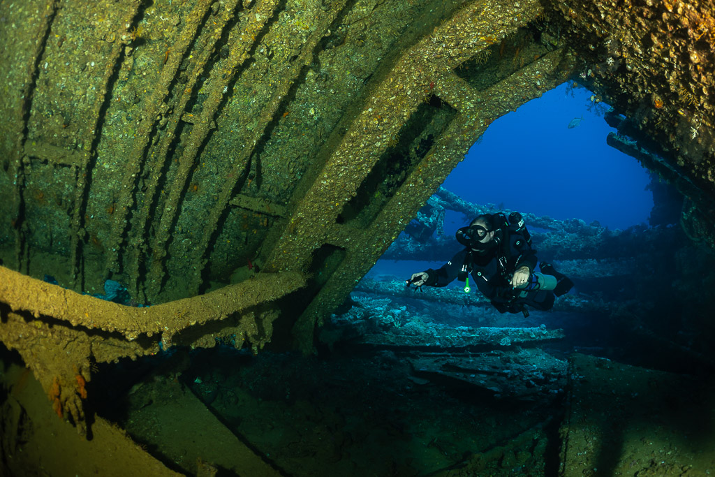 Rebreather diver framed by the rusty arch of a wreck hold, Red Sea, Egypt