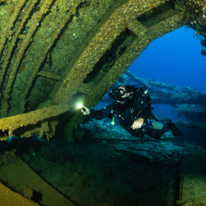 Rebreather diver with torch framed by the rusty arch of a wreck hold, Red Sea, Egypt