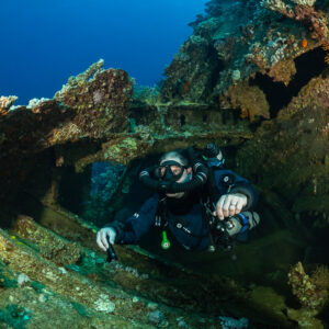 Rebreather diver emerging from twisted coral-covered wreck plating, Red Sea, Egypt