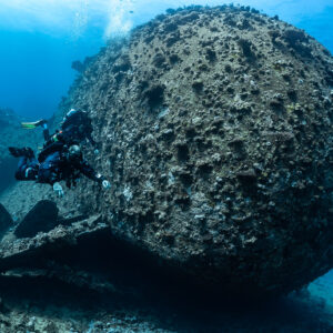 Rebreather diver close to the rounded coral-encrusted stern of a wreck, Red Sea, Egypt