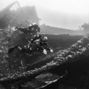 Black-and-white view of two divers along the tilted deck of a wreck, Red Sea, Egypt