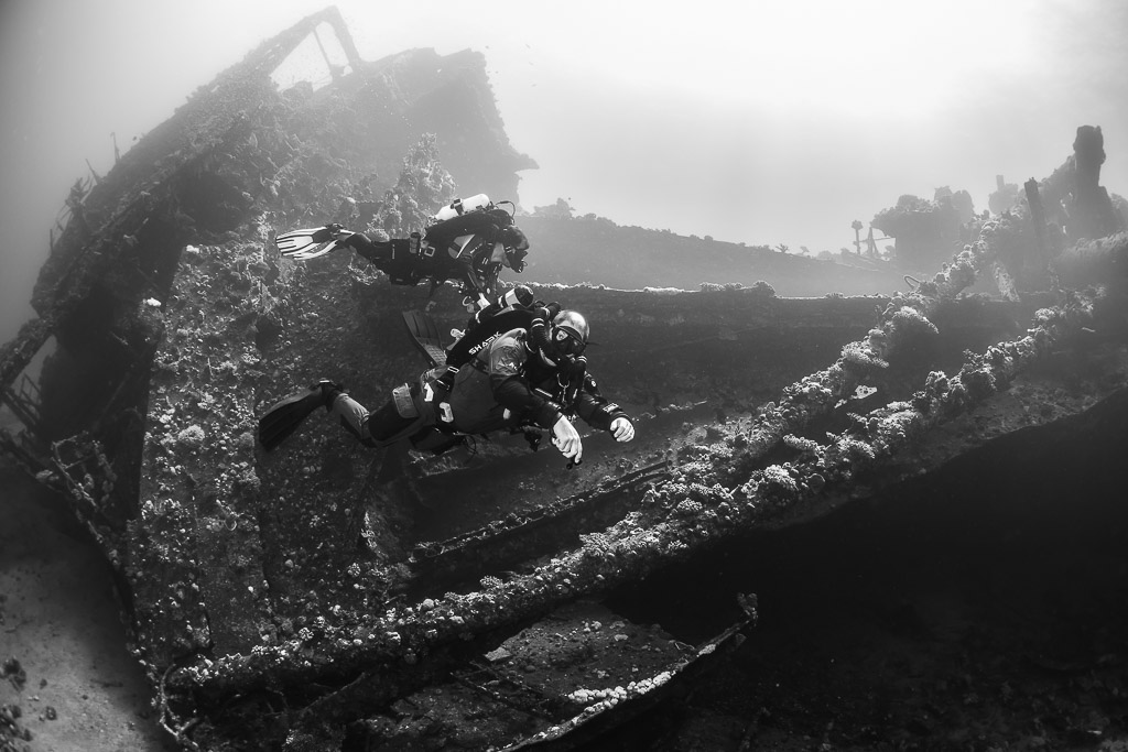 Black-and-white view of two divers along the tilted deck of a wreck, Red Sea, Egypt