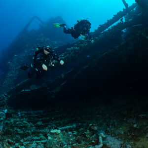 Two rebreather divers descending along the dark side of a wreck, Red Sea, Egypt