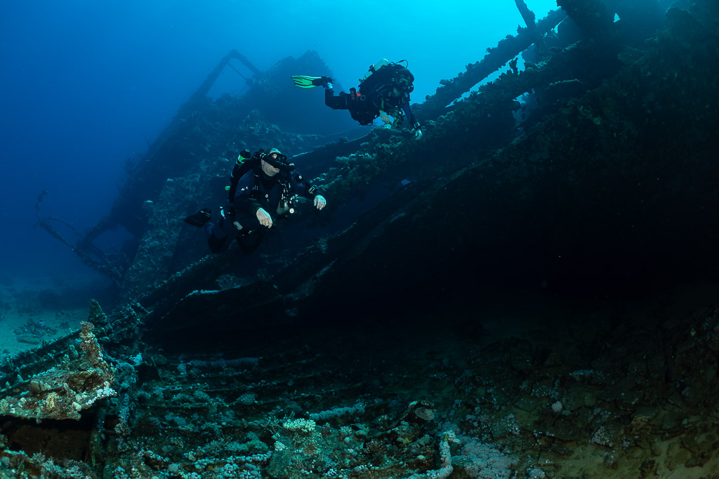 Two rebreather divers descending along the dark side of a wreck, Red Sea, Egypt