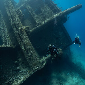 Two rebreather divers below cargo derricks on a wreck, vertical, Red Sea, Egypt