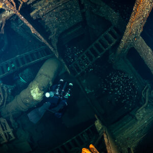 Rebreather diver with torch among pipes and girders of a wreck hold, Red Sea, Egypt