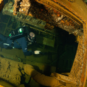 Rebreather diver swimming through a rusty hatch inside a wreck, Red Sea, Egypt