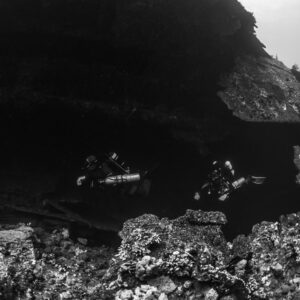 Black-and-white shot of two divers under a dark wreck overhang, Red Sea, Egypt