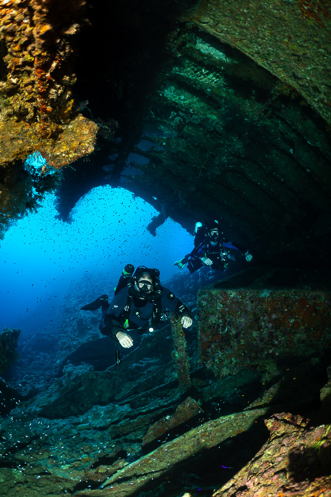 Rebreather diver in a wreck opening against blue water, vertical, Red Sea, Egypt