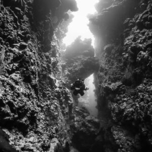 Black-and-white shot of a diver deep in a sunlit crevice, vertical, Red Sea, Egypt