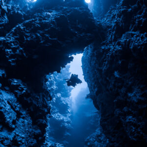 Silhouette bleutée d’un plongeur sous une arche rocheuse dans une faille, vertical, mer Rouge, Égypte