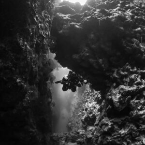 Black-and-white diver passing under a rock arch with light above, vertical, Red Sea, Egypt