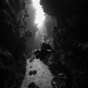 Black-and-white diver in a canyon with light streaming from above, vertical, Red Sea, Egypt