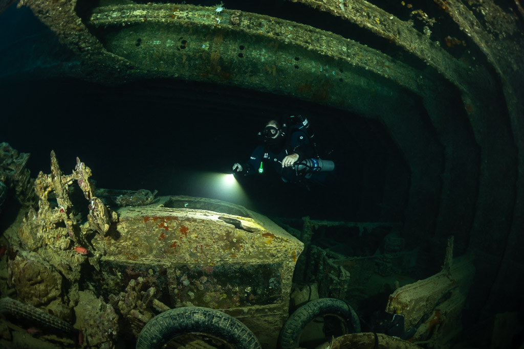 Rebreather diver lighting a truck cab in a dark cargo hold, Thistlegorm wreck, Red Sea, Egypt