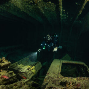 Rebreather diver lighting a truck cab and stacked cargo, Thistlegorm wreck, Red Sea, Egypt