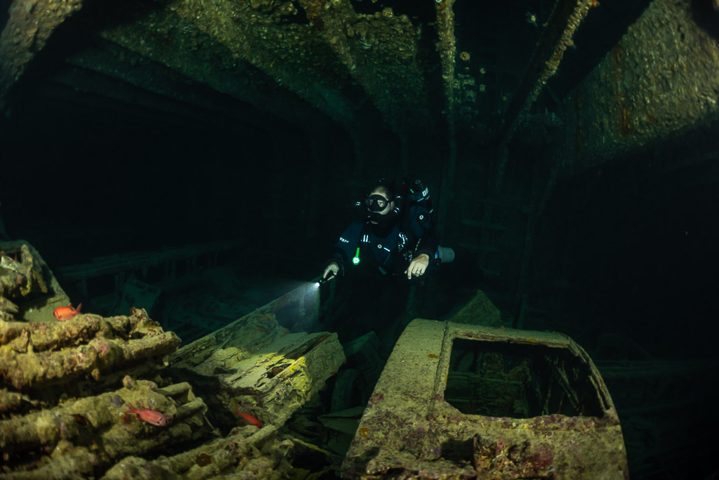 Rebreather diver lighting a truck cab and stacked cargo, Thistlegorm wreck, Red Sea, Egypt