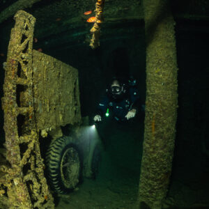 Rebreather diver lighting a truck between hold pillars, vertical, Thistlegorm wreck, Red Sea, Egypt
