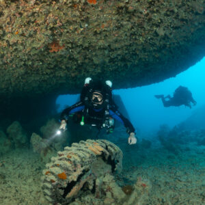 Rebreather diver under a wreck hull overhang with a tyre in front, Thistlegorm wreck, Red Sea, Egypt