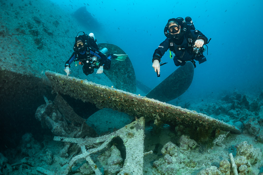 Two rebreather divers above a fallen plate near a wreck propeller, Thistlegorm wreck, Red Sea, Egypt