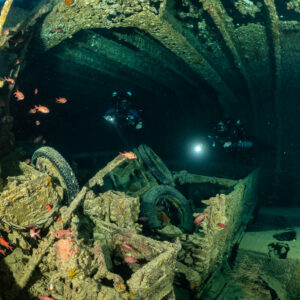 Two rebreather divers with torches beyond wheels and wreckage in a hold, Thistlegorm wreck, Red Sea, Egypt
