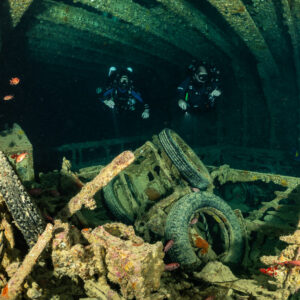 Two rebreather divers behind tyres and encrusted vehicles in a hold, Thistlegorm wreck, Red Sea, Egypt