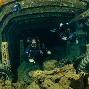 Two rebreather divers among tyres and cargo with a fish above, Thistlegorm wreck, Red Sea, Egypt