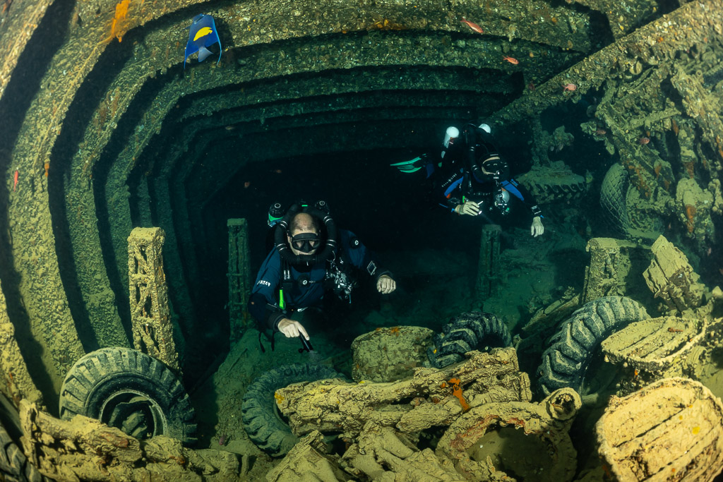 Two rebreather divers among tyres and cargo with a fish above, Thistlegorm wreck, Red Sea, Egypt
