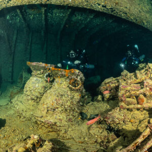 Two rebreather divers behind encrusted cargo and a lone tyre, Thistlegorm wreck, Red Sea, Egypt
