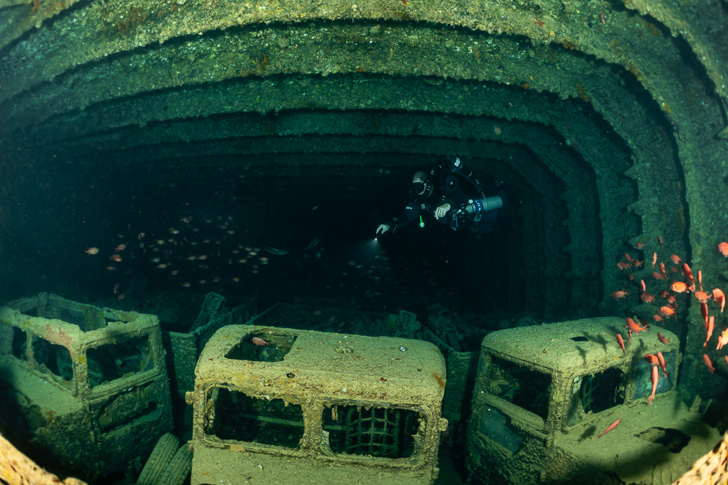 Rebreather diver above a row of three truck cabs in a hold, Thistlegorm wreck, Red Sea, Egypt