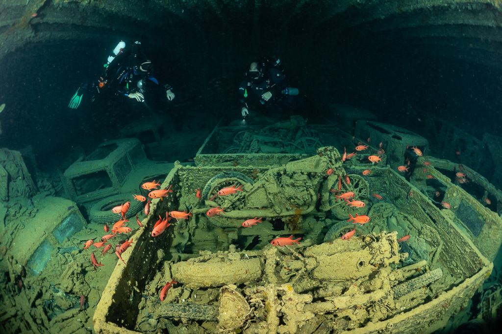 Benne de motos dans une cale avec poissons-soldats et plongeurs, plan plus large, épave du Thistlegorm, mer Rouge, Égypte