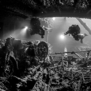 Black-and-white shot of two divers with torches above a motorcycle in a hold, Thistlegorm wreck, Red Sea, Egypt