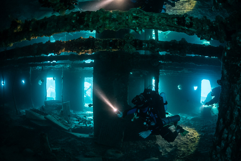 Rebreather diver with torch among pillars of a flooded wreck deck, Thistlegorm wreck, Red Sea, Egypt