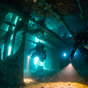 Two rebreather divers with torch beams inside a dark wreck deck, Thistlegorm wreck, Red Sea, Egypt