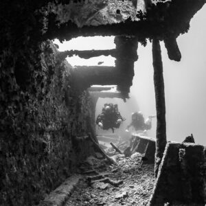 Black-and-white view of two divers in a long wreck corridor, vertical, Thistlegorm wreck, Red Sea, Egypt