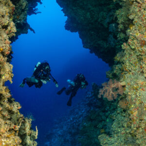 Two divers in a narrow reef crevice opening to blue water, vertical, Red Sea, Egypt